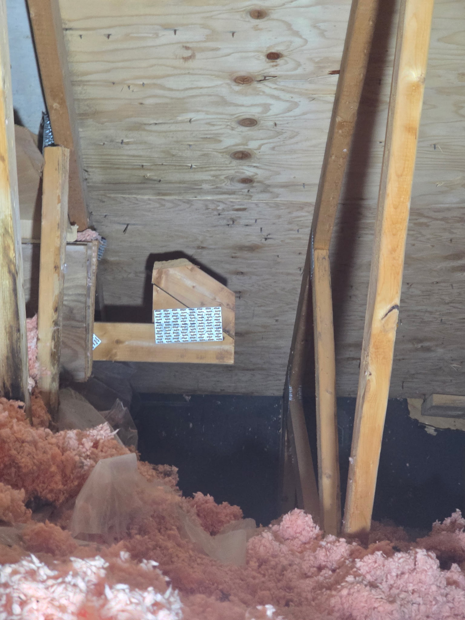 Isolant soufflé rose couvrant le plancher d'un entretoit, avec déflecteur de ventilation entre les chevrons